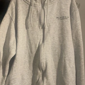 Grå hoodie från McKenzie - Säljer en grå hoodie från McKenzie i storlek XL. Den har en dragkedja framtill och en justerbar huva med snören. Perfekt för en avslappnad stil och passar bra till både höst och vår och även vintern. Hoodien är i bra skick och superbekväm att ha på sig. Pris går att diskutera!