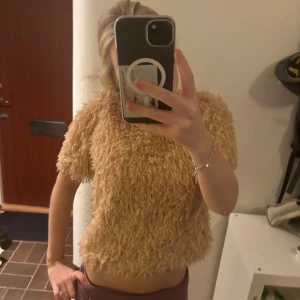 Beige fluffig tröja - Säljer en supersnygg beige fluffig topp. Den har korta ärmar och en croppad passform som ger en trendig look. Perfekt för höst och vår när du vill ha något bekvämt men ändå snyggt. Passar bra till både jeans och kjol!