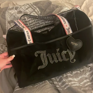 Svart väska från Juicy Couture - Säljer en superfin svart väska från Juicy Couture! Den har ett stort Juicy-tryck med glittriga detaljer på framsidan. Insidan är mönstrad med Juicy Couture-loggan och väskan har praktiska handtag med märkets namn,dels fack inuti väskan . Säljer pågrund av den inte används nyskick!! Priset kan diskuteras !