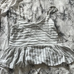 Randig topp från ASOS - Säljer en superfin randig topp från ASOS i storlek S. Den är gjord av 89% viskos och 11% bomull, vilket gör den både mjuk och bekväm. Toppen har smala axelband och en volangdetalj längst ner.