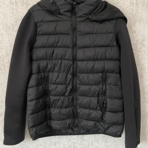 Svart pufferjacka från Zara - Säljer en snygg svart pufferjacka från Zara i storlek S. Jackan har en quiltad design med dragkedja framtill och två praktiska fickor med dragkedjor. Perfekt för höst och vinter, håller dig varm och stilren. Den har långa ärmar och en huva för extra skydd mot kylan. På bild 2 har jag vikt upp jackan lite men som man ser på bild 1 så är den längre och går ner till början av höften ungefär.