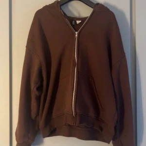 Brun hoodie med dragkedja - Säljer en mysig brun hoodie med dragkedja framtill. Den har en avslappnad passform och långa ärmar, perfekt för höst och vinter. Superbekväm och lätt att matcha med andra plagg!