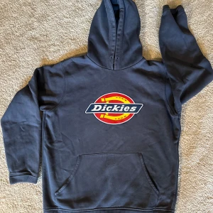 Svart hoodie från Dickies - Säljer en blå hoodie från Dickies med deras ikoniska logga i rött och gult på bröstet. Den är superbekväm och perfekt för både höst och vinter. Har en stor ficka fram och en mysig huva. Perfekt för chill dagar eller när du vill ha en avslappnad stil.