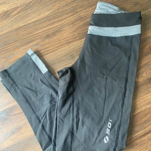 Svarta leggings med grå detaljer - Säljer ett par svarta leggings med grå midja och detaljer. Perfekta för träning eller en avslappnad dag. De är i relativt bra skick och superbekväma!