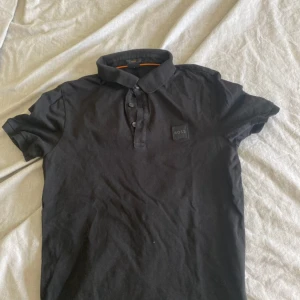 Svart kortärmad pikétröja från BOSS - Säljer en stilren svart pikétröja från BOSS i slim fit. Tröjan har en klassisk krage med knappar och är perfekt för både vardag och fest. Den är i bra skick och redo för en ny ägare! nypris 1000 men vårt pris 299kr.