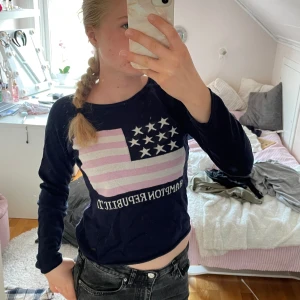 Mörkblå tröja med flaggmönster - Säljer en snygg mörkblå tröja från Hampton Republic med ett coolt flaggmönster i rosa och vitt på framsidan. Tröjan är långärmad och perfekt för en casual look. Den är i bra skick och passar perfekt till jeans!