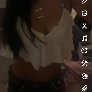 Vit broderad linne topp - Säljer en superfin vit linne topp med spets detaljer. Toppen är ärmlös och har en söt volangkant längst ner. Perfekt för sommardagar🥰 Den har en v-ringad design och smala axelband som knyts på axlarna.