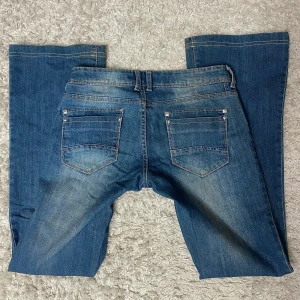 Blå lågmidjade jeans - Så snygga lågmidjade jeans som är stretchiga!  Dom har unika nitar längst fickorna, tyvärr har en lossnat på ena bak fickan men inget som syns!  Midjemått: 38 x 2 Innebenslängd: 83cm