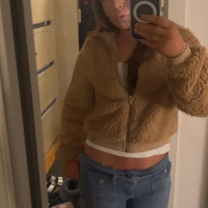 Beige teddyjacka - Mysig beige teddyjacka med dragkedja framtill. Jackan är i fint skick och kan användas både som jacka men även som en snygg kofta för kalla dagar. Den fluffiga texturen ger en trendig look.