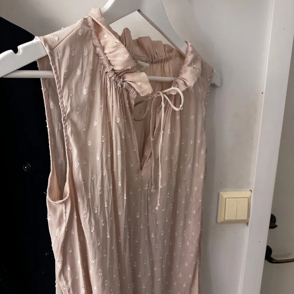 Säljer en söt ljusrosa ärmlös topp från H&M med diskret mönster och knytband vid halsen. Perfekt för varma dagar och ger en romantisk touch till din stil. 💕. Yläosat.