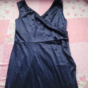 Mörkblå omlottklänning - Lånh elegant mörkblå omlottklänning i satin med v-ringad hals och slits. Perfekt för en stilren look.