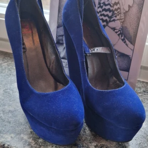 Blå platform pumps med kilklack - Höga blå pumps i mocka med kilklack och platå. De är från 2010-talet men aldrig använda så de är i gott skick! Finns ett band runt ankeln för stabilitet. :) 