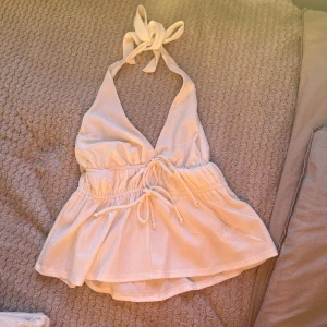 Vit halterneck topp från BikBok - Säljer en söt vit halterneck topp från BikBok. Toppen har en knytning i nacken och en volangdetalj vid midjan. Storlek M men passar S