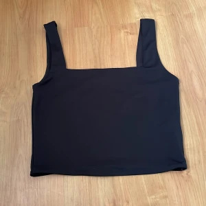 Svart ärmlös topp - Snygg svart ärmlös topp med breda axelband. Perfekt för en stilren look. Passar bra till både jeans och kjol.