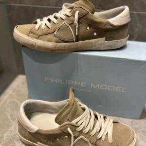 Beige sneakers från Philippe Model - Snygga beige sneakers från Philippe Model i mocka med vita detaljer. Skorna har en klassisk design med snörning och en bekväm passform. Perfekta för en stilren look.