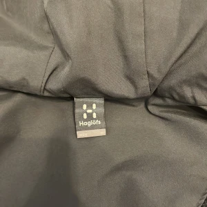 Blå regnjacka från Haglöfs - Säljer en blå regnjacka från Haglöfs i storlek M. Jackan har en praktisk huva och dragkedja framtill. Perfekt för regniga dagar och håller dig torr och bekväm. Haglöfs-loggan syns på bröstet.