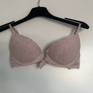Rosa spets-bh från H&M - Mycket använd, men sparsamt använd. Säljer en söt rosa bh från H&M i spets med dekorativ rosett mellan kuporna. Perfekt för en romantisk look. Justerbara axelband för bästa passform.