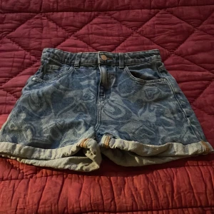 Hjärtmönstrade jeansshorts - Snygga jeansshorts med ett fint hjärtmönster i blått. De har en klassisk femficksdesign och uppvikta benslut för en avslappnad look. Perfekta för sommarens äventyr!