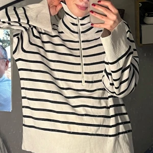 Randig tröja med dragkedja - Säljer en stilren vit och svart randig tröja med dragkedja. Tröjan har långa ärmar och en hög krage som kan justeras med dragkedjan. Perfekt för en avslappnad look. Finns en liten skavank, skriv privat för bild!