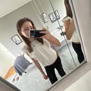 Vit blus med volangdetaljer - Säljer en söt vit blus med volangdetaljer på ärmarna. Blusen har en lös passform och är perfekt för en avslappnad stil. Den är ärmlös och har en rund halsringning.