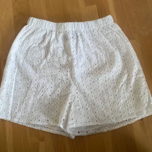 Vita shorts med hålmönster! - Snygga vita shorts från Boohoo med broderade detaljer, nästan blommor. De har en elastisk midja för extra komfort och är perfekta för varma sommardagar. Shortsen är tillverkade i ett lätt och luftigt material utan att vara genomskinliga. Shortsen har även ett tunt undertyg för att de inte ska vara genomskinliga. 