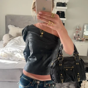 Svart oneshoulder topp - Snygg svart oneshoulder topp i syntetmaterial med trekvartsärm. Perfekt för en trendig look med en unik asymmetrisk design. I fejk skinn💓