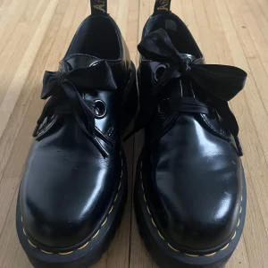 Dr. Martens med snörning och rosett - Snygga svarta Dr. Martens skor i skinn med snörning och dekorativa rosetter. De har den klassiska gula sömmen runt sulan och en robust design. Perfekta för en stilren look. Det står 39 i dem men jag har 39 och de är så stora att de åker av när jag går, så jag skulle säga 41 eller minst 40.