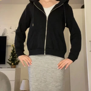 Svart hoodie med dragkedja - Säljer en stilren svart hoodie med dragkedja och huva. Perfekt för en avslappnad look. Den har långa ärmar och en bekväm passform.