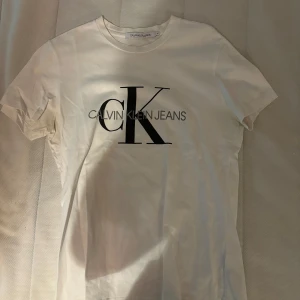 Vit t-shirt från Calvin Klein Jeans - Snygg vit t-shirt från Calvin Klein Jeans med det ikoniska CK-logotypen tryckt i svart på framsidan. Perfekt för en stilren och avslappnad look.