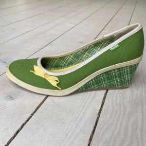 Gröna kilklackar från Keds - Söta gröna kilklackar från Keds med en gul rosett på ovansidan. Skorna har ett rutigt mönster på kilklacken och en bekväm vadderad insida i gult. Något gulnad vit kant runtom, men det ser nästan ut som att det ska vara så eftersom skorna går i grönt och gult. Storlek 38 (7,5) Använda ett fåtal gånger. 
