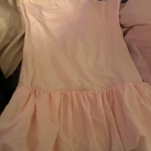 Ljusrosa klänning med volangdetaljer - Söt ljusrosa klänning med volangdetaljer i nederkant. Perfekt för en somrig look. Klänningen har en mjuk och luftig känsla. Använd en gång och är liten i storlek!