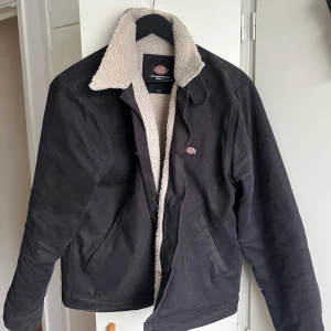 Svart jacka med teddyfoder från Dickies - Säljer en svart arbetsjacka från Dickies med mysigt teddyfoder. Jackan har en klassisk design med knappar och en varm krage. Ser sliten ut men går att tvätta bort skavanker ☺️