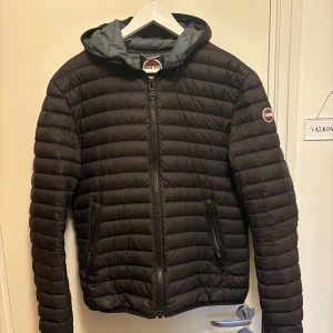 Svart pufferjacka från Colmar - Säljer en svart pufferjacka från Colmar med dragkedja och huva. Jackan har en quiltad design och är perfekt för vår väder. Den har långa ärmar och praktiska fickor med dragkedja.