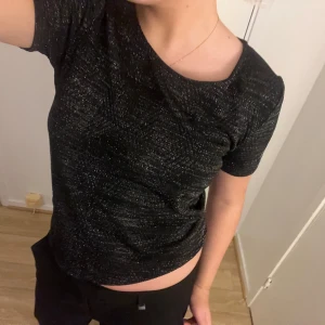 Svart glittrig topp - Snygg svart glittrig topp med korta ärmar. Perfekt för en kväll ute eller en festlig tillställning. Toppen har en bekväm passform och ett glittrande mönster som ger en extra touch av glamour.