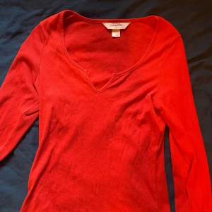 Röd ribbad tröja från Hunkemöller - Snygg röd ribbad tröja från Hunkemöller med v-ringning. Perfekt för en stilren look. Tröjan har långa ärmar och är tillverkad i ett mjukt material som ger en bekväm passform. Inte använd en ända gång,