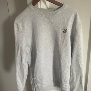 Grå tröja från Lyle & Scott - Säljer en stilren och bekväm grå tröja från Lyle & Scott. Den har en klassisk design med ett litet broderat emblem på bröstet. Perfekt för både vardag och avslappnade tillfällen.