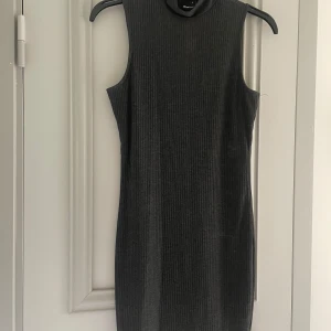 Grå ribbad klänning från Gina Tricot - Säljer en snygg grå ribbad klänning från Gina Tricot. Den är ärmlös och har en hög krage, perfekt för både vardag och fest. Klänningen är i storlek S och har en tight passform som framhäver figuren. Superbekväm och stilren!