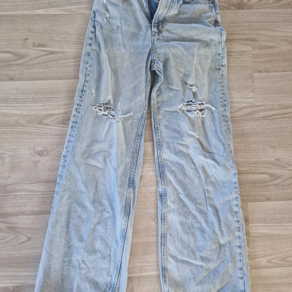 Säljer ett par ljusa jeans från Divided i storlek XS. De har en avslappnad passform med slitna detaljer på knäna för en cool look. Perfekta för en casual outfit!. Jeans & Byxor.