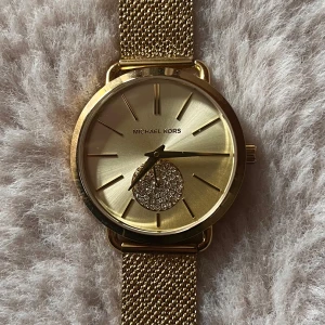 Guldfärgad klocka från Michael Kors - Säljer pga urtavla för stor för min handled. Elegant guldfärgad klocka från Michael Kors modell Portia MK3844. Klockan har en stilren design med zirconia stenar på urtavlan och ett mesh-armband i guld. Klockan är i helt nyskick! 