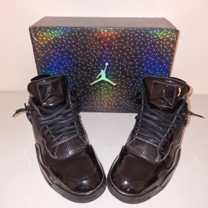 Air Jordan 4 Retro 11Lab4 Black 2015 - Säljer ett par svarta Nike Air Jordans i glänsande skinn. De har en cool design med snörning och en robust sula. Skorna är i bra skick och kommer med originalkartongen som har ett snyggt geometriskt mönster.