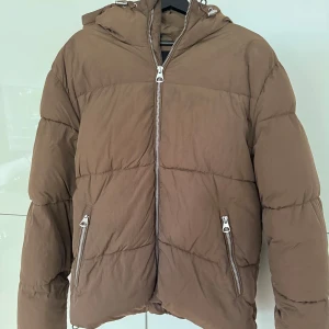 Brun dunjacka - Brun dunjacka, i princip oanvänd från H&M. Väldigt bekväm och varm jacka, perfekt till vintern eller kalla höstpromenader. Inga tecken på användning, hör av dig vid frågor!