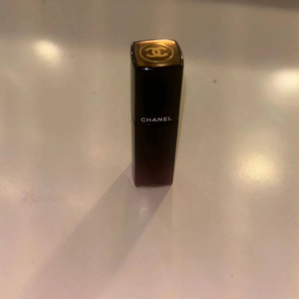 Säljer ett elegant Chanel Rouge Allure Laque läppstift i nyansen 80. Det är en lyxig flytande läppfärg med en intensiv röd ton. Perfekt för en glamorös look! Förpackningen är stilren och svart med den ikoniska Chanel-loggan på toppen. Jätte pigmenterad!. Skönhet.