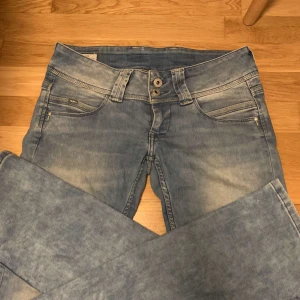 Blå jeans från Pepe Jeans - Säljer ett par snygga ljusblå jeans från Pepe Jeans i straight modell. De är lågmidjade och har en klassisk femficksdesign. Perfekta för en avslappnad vardagslook. Jeansens slitna look ger dem en cool vintagekänsla.