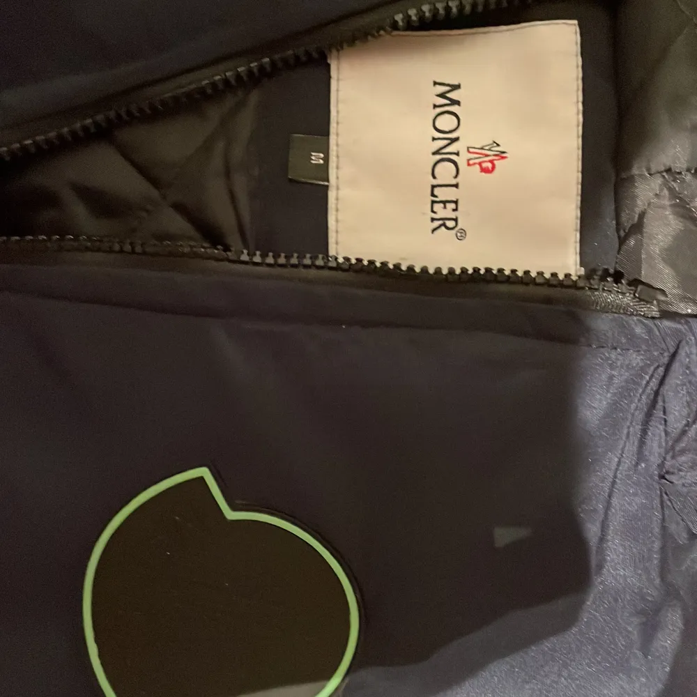 Säljer en snygg mörkblå vindjacka från Moncler. Jackan har en dragkedja framtill och ett stilrent Moncler-märke på bröstet. Perfekt för blåsiga dagar och har en skön passform. Passar både till vardags och lite mer uppklädda tillfällen. 🌀. Jackor.