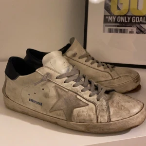 Golden Goose sneakers i vitt och svart - Säljer ett par Golden Goose sneakers. Ganska slitna med ett hål i sulan som skulle kunna limmas eller fixa proffesionellt.