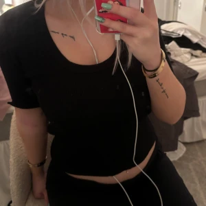 Svart ribbad topp - Säljer en snygg svart ribbad topp med korta ärmar. Den är croppad och har en bekväm passform som passar perfekt till både vardag och fest. Toppen är i bra skick och kan enkelt matchas med olika outfits. Har haft ett hål i armhålan som är igensytt 