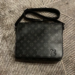 Svart axelväska från Louis Vuitton - Säljer en snygg svart axelväska från Louis Vuitton i skinn med det klassiska monogrammönstret. Väskan har en justerbar axelrem och är perfekt för både vardag och fest. Den är i mycket bra skick och har gott om plats för dina saker. Perfekt för dig som vill ha stil och funktion i ett!