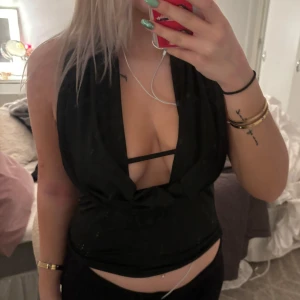 Svart halterneck topp - Snygg svart halterneck topp med djup urringning och smala axelband. Perfekt för en utekväll eller fest. Toppen är tight och framhäver figuren på ett stilrent sätt.