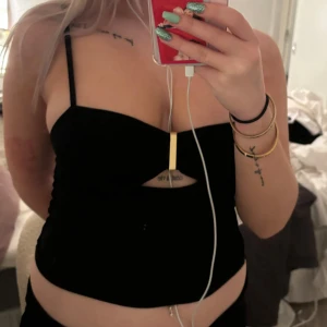 Svart axelbandslös topp - Snygg svart topp med smala axelband och en dekorativ metallring framtill. Perfekt för en utekväll eller fest. Toppen är tight och framhäver figuren på ett stilrent sätt. Har i både mörkblå och svart färg, skriv för mer bilder