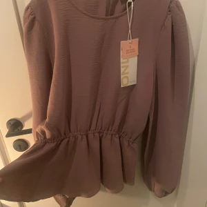 Långärmad topp från ONLY i färgen Elderberry - Säljer en superfin långärmad blus från ONLY i en elderberry-färg. Blusen har intagen midja och med en knapp där back i halsen.  Helt ny med tag kvar, köptes för 400 kr.